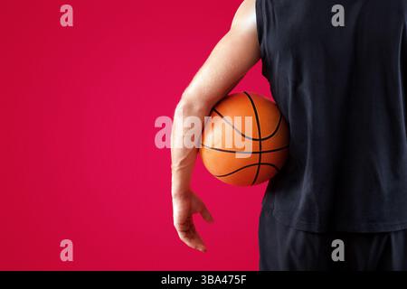 Gros plan d'un joueur de basket-ball du millénaire tenant le ballon sur fond rouge du studio, espace pour le texte Banque D'Images