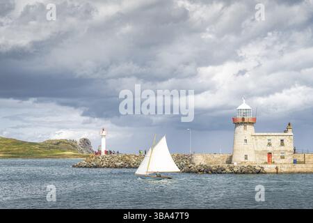 Les gens sur un petit voilier sortant de la marina de Howth, passant Howth Lighthouse et Per, avec l'île Irelands Eye en arrière-plan, Dublin, Irlande, Europe Banque D'Images
