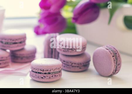Violet doux macarons délicieux et tulipes fraîches sur fond blanc. Faible profondeur de champ. Coloration de la photo tonique Banque D'Images