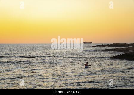 Deux filles s'assoient à bord dans la mer méditerranée tranquille au coucher du soleil dans la ville de paphos à chypre. Silhouettes de 2 filles pagayant sur paddle board à Banque D'Images