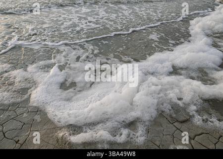 Mousse blanche s'accumulant sur le rivage d'un lac ondulé. Banque D'Images
