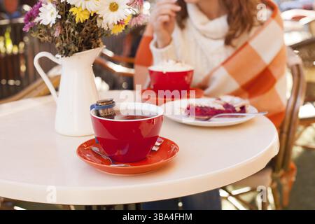 La femme est assise dans un café extérieur et mange du gâteau et du cacao, un automne confortable Banque D'Images