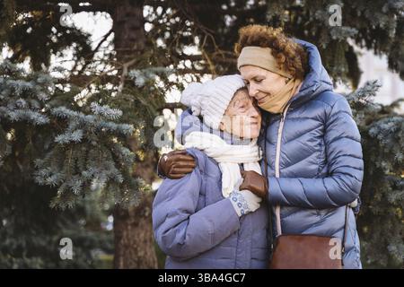 Couple de femmes d'âge mûr caucasien et de femmes âgées sont heureux de passer du temps sur les vacances de Noël et de nouvel an ensemble, souriant et embrassant dans la forêt Banque D'Images