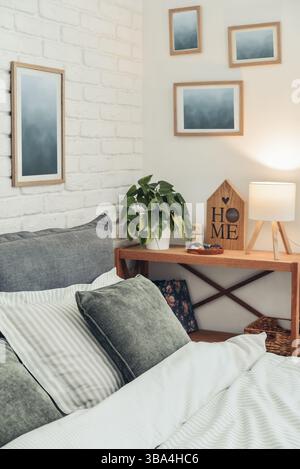 Intérieur élégant de la chambre avec grand lit gris confortable, plaid moutarde en lin et table de chevet en bois près du mur de briques blanches Banque D'Images