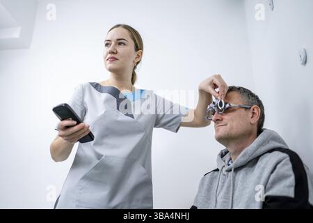 Correction de la vision.Sélection de lunettes.Des cadres d'essai professionnels sur le visage d'un patient mâle tandis que le médecin vérifie la vue chez un ophtalmologiste moderne Banque D'Images