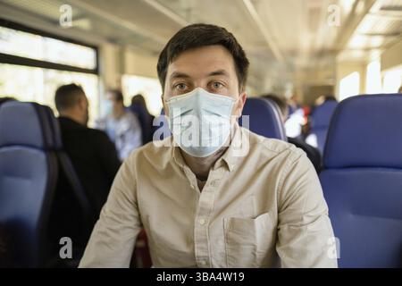Homme passager portant un masque facial pendant le verrouillage Covid-19 à l'intérieur du train. Nouveau concept de mode de vie normal. Prise de distance sociale lors de voyages en transports publics Banque D'Images
