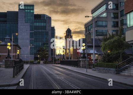 Belle architecture de bâtiments moder et vintage. Lampadaires illuminés au coucher du soleil sur George Dock Street avec des lignes de tramway, Dublin, Irlande, Europe Banque D'Images