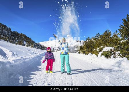 Mère et fille, famille, jetant de la neige poudreuse dans l'air, la forêt et les montagnes en arrière-plan. Vacances d'hiver au ski, El Tarter, Andorre, Pyrénées Banque D'Images