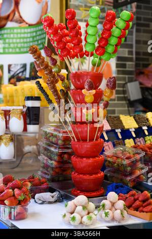 Un stand coloré de Street food à Shanghai présente des fruits traditionnels chinois confits sur des bâtonnets (tanghulu) - pommes glacées, fraises et agrumes Banque D'Images