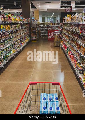 Balikpapan, Indonésie – 13 avril 2025. Un chariot avec des boîtes de lait UHT dans une allée de supermarché rempli de collations et de biscuits emballés. Banque D'Images