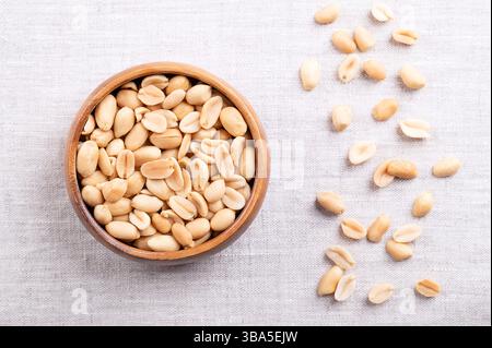 Cacahuètes grillées dans un bol en bois sur tissu de lin. Snack croquant prêt-à-manger à base de fruits d'Arachis hypogaea. Noix de grignotage dorées légères. Banque D'Images