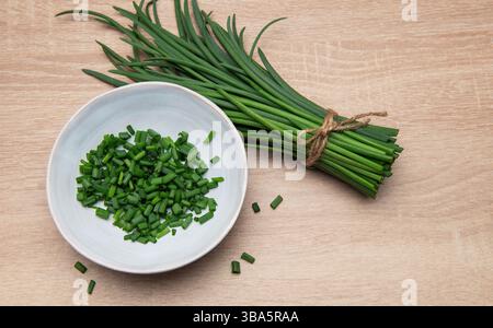 Ciboulette fraîche groupée et hachée dans un bol sur une surface en bois Banque D'Images