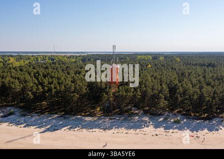 Une tour de communication se dresse au milieu d'une forêt dense près d'une plage de sable sereine par une journée ensoleillée. Banque D'Images