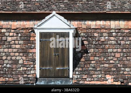 Lucarne vintage avec volets en bois fermés sur toit en tuiles rustiques en terre cuite vieillie Banque D'Images