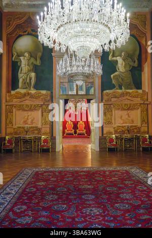 Lisbonne, Portugal - 5 mai 2025. Grande salle éclairée par un lustre au palais national d'Ajuda avec des peintures murales de l'Atlas et une vue sur la salle royale du trône rouge. Banque D'Images