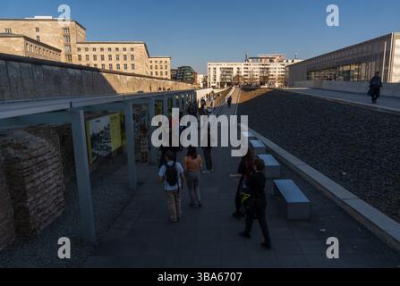 Une ouverture déchiquetée dans le mur d'excavation érodé révèle une grille en fil de fer et une silhouette marchant au-delà à la Topographie de la Terreur à Berlin, en Allemagne. Banque D'Images