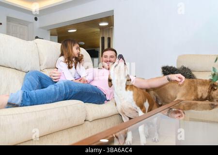 Mère enceinte, père et fille appréciant le temps de qualité avec leurs chiens sur un canapé confortable dans leur salon moderne Banque D'Images