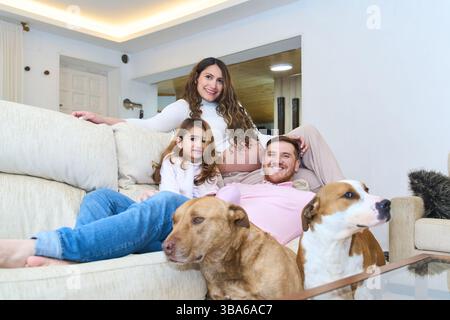 Mère enceinte, père, fille et chiens se relaxant ensemble sur un canapé confortable dans un salon moderne, profitant du temps en famille Banque D'Images