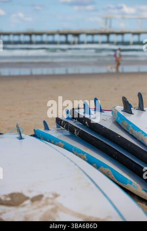 Planches de surf empilées sur la plage avec océan et jetée en arrière-plan Banque D'Images