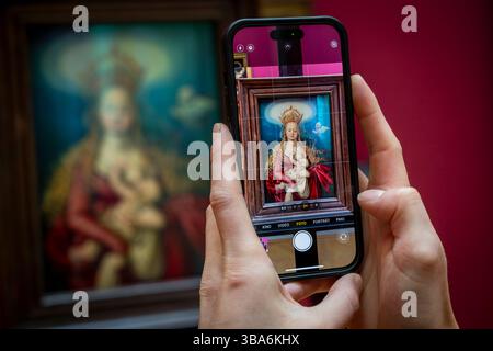 Munich, Allemagne. 12 mai 2025. Une femme photographie la nouvelle acquisition de l’Alte Pinakothek après une conférence de presse. Le tableau intitulé 'Marie reine du ciel' a été créé vers 1516/1518, mesure 35 centimètres sur 25,5 centimètres et a été peint par Hans Baldung (1484/85 - 1545). Crédit : Peter Kneffel/dpa/Alamy Live News Banque D'Images