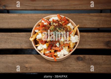 Poutine frites avec des fromages et du chorizo dans un récipient de sortie de papier. Délicieux repas fraîchement préparé, parfait pour les menus, les restaurants ou la livraison de nourriture con Banque D'Images