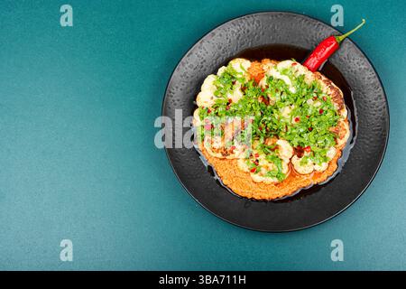 Les bouquets de chou-fleur rôtis sont arrosés de sauce tahini crémeuse et saupoudrés de graines de grenade. Copier l'espace. Banque D'Images