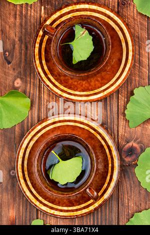 Une tasse de tisane, feuilles de Ginkgo biloba vert sur un fond en bois rustique. Banque D'Images