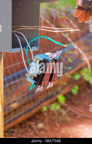 Une personne connecte les fils électriques à la boîte de jonction dans le cadre de jardin sous la journée de travail Banque D'Images