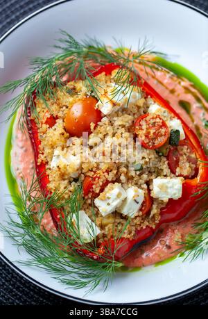 Poivron rouge rôti débordant de couscous aux herbes, feta émiettée, courgettes, tomates cerises, garni de sauce crémeuse à l'aneth sur une assiette rustique Banque D'Images