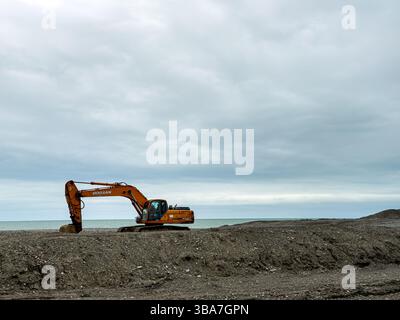 Excavatrice sur le site de construction côtier sous ciel nuageux, plan large, pas de gens. Concept industriel, d'infrastructure et d'aménagement du territoire. Banque D'Images