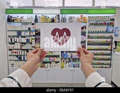 Mains de pharmacien féminin tenant un papier avec un symbole de coeur et un électrocardiogramme à l'intérieur. Concept de santé et de bien-être humain. Assurance maladie Banque D'Images