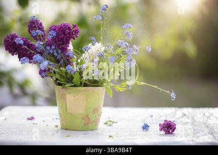 Fond de printemps ou d'été. Un bouquet de fleurs sauvages dans un vieux pot de fleurs, illuminé par la lumière du soleil. Belles fleurs sur un fond vert Banque D'Images