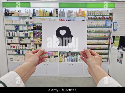 Mains de pharmacien tenant un papier avec une silhouette de tête avec un coeur à l'intérieur, symbolisant la santé mentale et le bien-être, sur les étagères de la pharmacie backdr Banque D'Images
