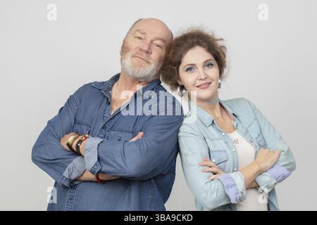 Une fille adulte avec un père âgé en vêtements denim posant et regardant la caméra. Belle-fille et beau-père sur fond gris Banque D'Images