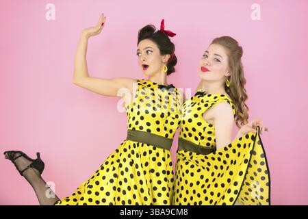 Les filles rétro. Deux femmes en robes jaunes sur un fond rose Banque D'Images
