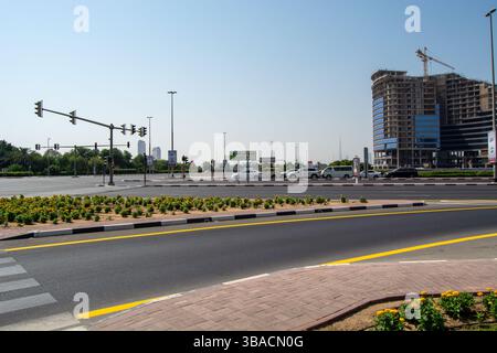 Une intersection urbaine animée avec des feux de circulation, une route bien entretenue et un parterre de fleurs. En arrière-plan, un chantier de construction et des buildi modernes Banque D'Images
