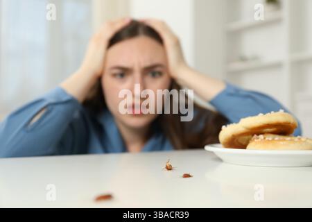 Jeune femme choquée regardant des cafards et des bretzels sur une table blanche à l'intérieur, mise au point sélective. Problème de ravageur Banque D'Images