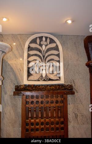 Un élément mural décoratif avec un motif floral en noir et blanc, placé sur un fond de pierre texturé. En dessous, un panneau en bois avec env. Complexe Banque D'Images