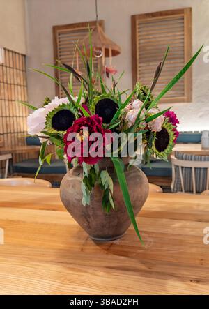 Décor de table du restaurant : fleurs mélangées, y compris pivoines en faïence pot sur surface en bois. Disposition pivoine et tournesol vibrante dans un vase rustique Banque D'Images