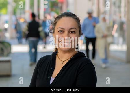 Une belle femme souriante debout contre une toile de fond de bâtiments de la ville par une journée ensoleillée Banque D'Images