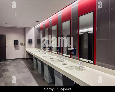 Toilettes publiques modernes avec un long comptoir, plusieurs éviers, miroirs, robinets automatiques et sèche-mains. Nettoyer l'intérieur d'un support commercial vide Banque D'Images