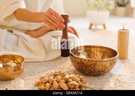 Gros plan d'une femme utilisant un bol chantant tibétain lors d'une séance de guérison sonore à la maison, dans une lumière chaude paisible. Banque D'Images
