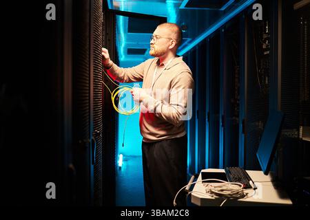 Technicien connectant les câbles réseau dans la salle des serveurs Banque D'Images