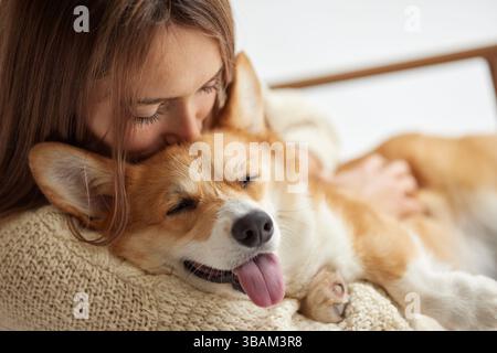 Heureux chien Corgi dormant paisiblement dans les bras de la femme, câlin chaud confortable, montrant l'amour, la confiance et la détente. Banque D'Images