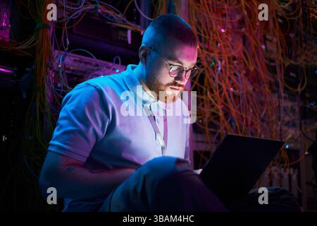 Portrait d'homme barbu travaillant sur ordinateur portable dans la salle de serveur Banque D'Images