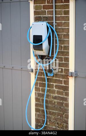 Pays-Bas : borne de recharge pour véhicules électriques montée sur un mur de garage en briques vintage, avec câble bleu, montrant l'infrastructure locale des véhicules électriques dans un histo néerlandais Banque D'Images