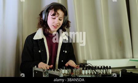 Une fille se penche sur une table d'harmonie, ses mains sur les commandes et un sourire sur son visage. Cette image capture la joie de l'implication créative dans la musique ou Banque D'Images