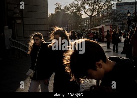 Les gens marchant dans une rue de Barcelone, en Espagne, par une journée très venteuse, avec de fortes rafales, des silhouettes rétro-éclairées et la lumière du soleil l'après-midi. Banque D'Images