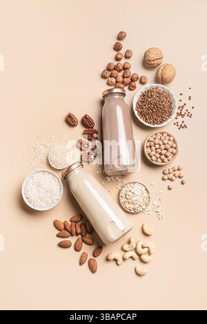Bouteilles de lait végétaliennes et ingrédients. Non laitier, lait sans lactose avec des noix et des grains sur fond beige, vue de dessus. Boisson de substitution, lui Banque D'Images
