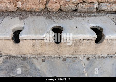 Rangée de toilettes romaines en pierre à Éphèse, avec des sièges en forme de trou de serrure utilisés communalement, une partie des anciens systèmes d'assainissement public. Banque D'Images